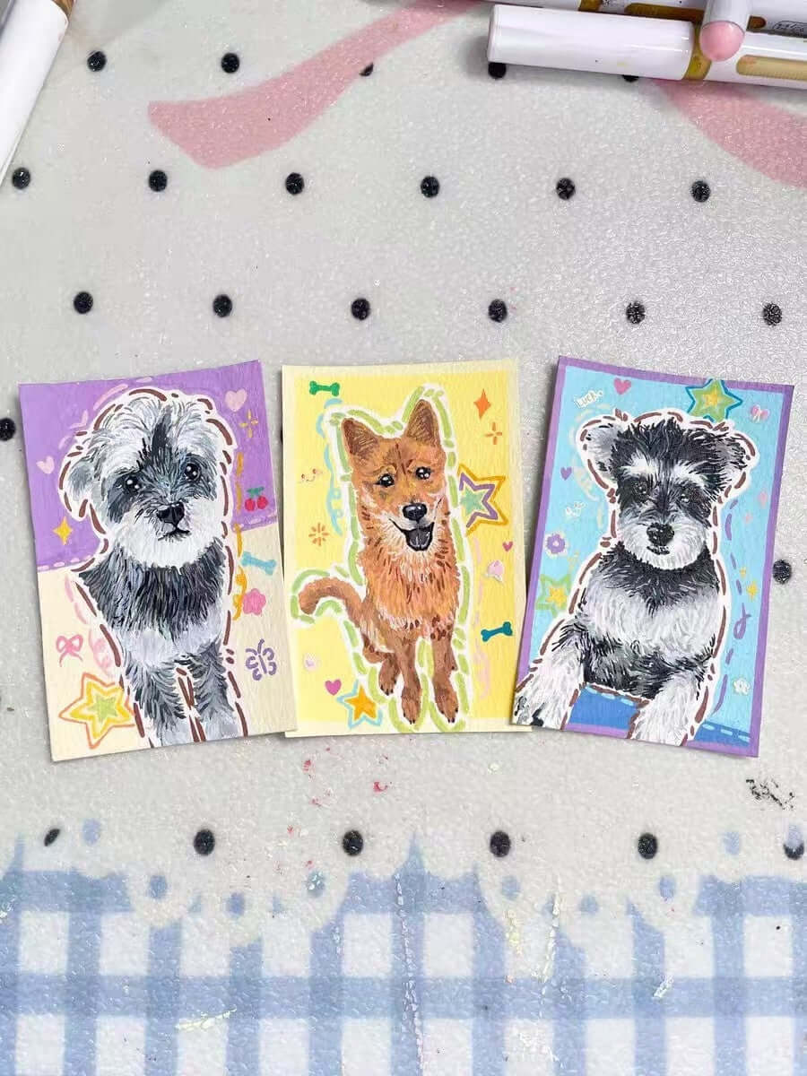Three hand-painted dog portrait cards on an artist’s worktable